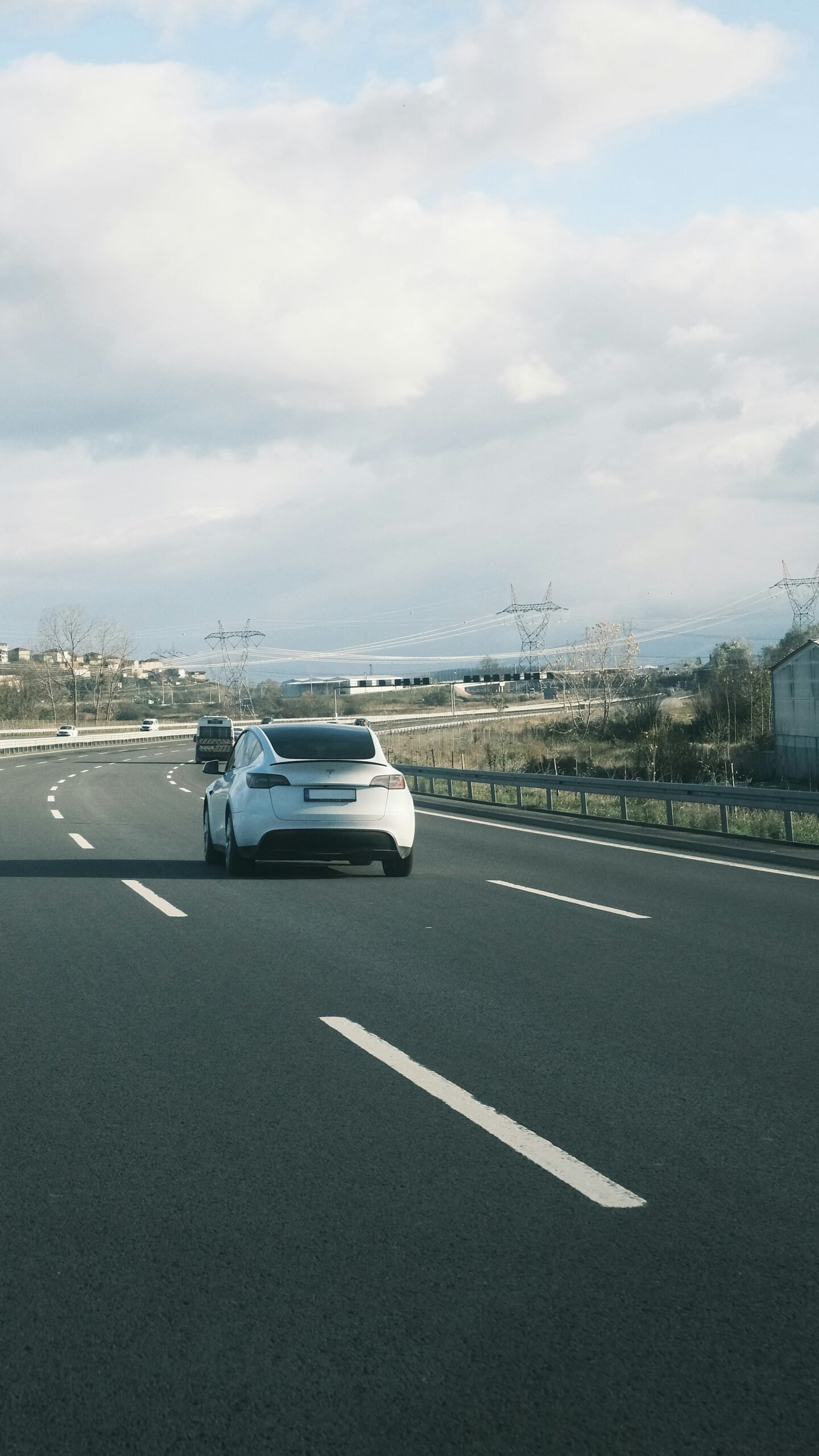 A white car driving down a highway with a sky background